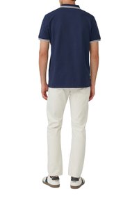 Marineblaues Poloshirt mit weißem Besatz am Kragen und den Ärmeln, kombiniert mit hellcremefarbenen Hosen und weißen Sneakers mit braunen Akzenten.