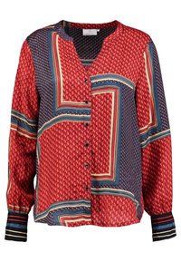 Blouse rouge à motifs avec un col en V, ouverture à boutons, manches longues, et un mélange de motifs géométriques et pois en accents bleu et crème.