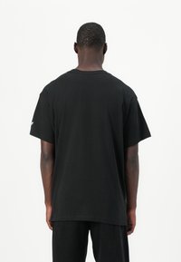 Μαύρη κοντομάνικη μπλούζα φτιαγμένη από βαμβάκι, με κλασικό λαιμόκοψη, άνετη εφαρμογή και λεία πλάτη χωρίς εμφανή λογότυπα ή σχέδια.