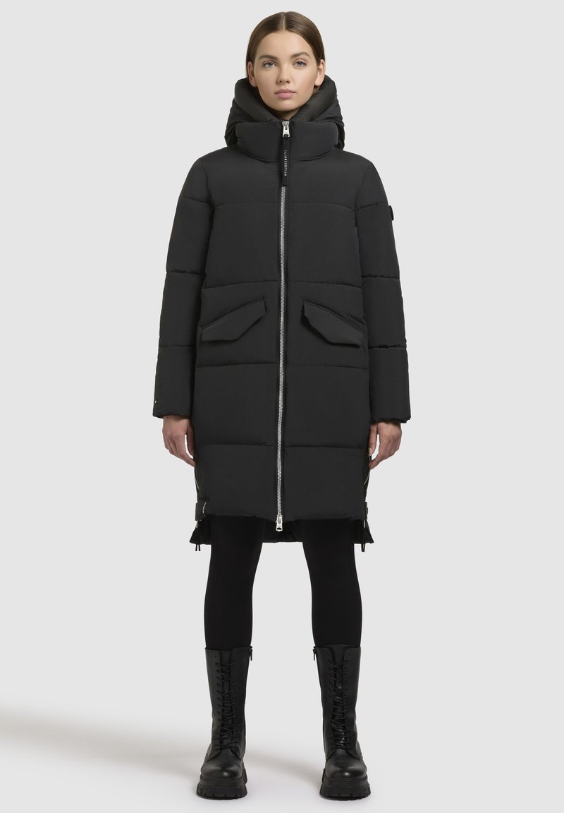 Schwarze Daunenjacke mit hohem Kragen und Reißverschluss, ausgestattet mit zwei Fronttaschen und einem knielangen Design. Strukturierte, matte Oberfläche.