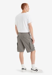 Pantaloni cargo grigi con tasche laterali, abbinati a una maglietta bianca e sneakers bianche. I pantaloni presentano una vestibilità comoda e dettagli di cucitura in vista.