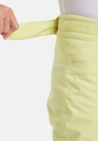 Lichtgele broek met een klittenbandsluiting en een geborduurd logo op de onderkant van de linkerpijp. Gladde textuur met een getailleerde pasvorm.