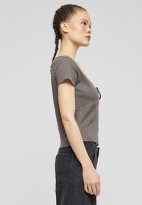 Grå ribbet topp med tettsittende design, kort erm, og V-hals, kombinert med høyt liv mørke jeans med sidelommer.
