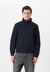 Giacca blu navy realizzata in tessuto liscio e leggero. Presenta un colletto alto, una cerniera frontale e tasche con zip. Maniche e orlo a coste.