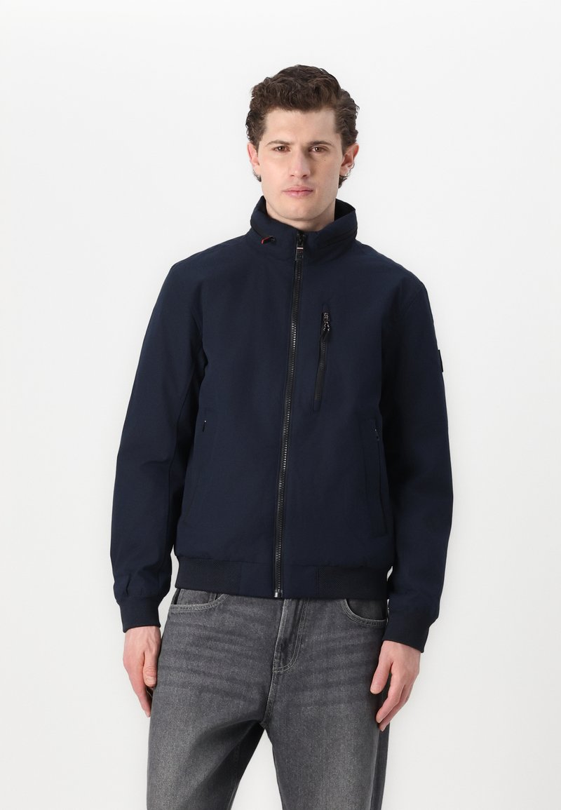 Giacca blu navy realizzata in tessuto liscio e leggero. Presenta un colletto alto, una cerniera frontale e tasche con zip. Maniche e orlo a coste.