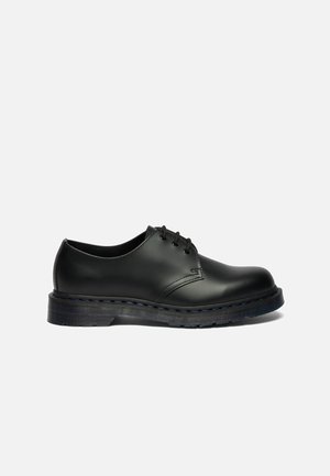 Chaussure habillée en cuir noir à lacets avec une semelle épaisse et des détails cousus, vue de profil sur un fond gris uni.