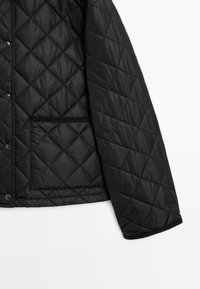 Black quilted jacket featuring a diamond pattern, snap buttons, and a side pocket with a textured trim. Smooth, insulated material.