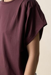 Bordeauxrood katoenen T-shirt met een losse pasvorm en korte mouwen. Voorzien van een eenvoudige ronde hals en een gladde, zachte textuur.