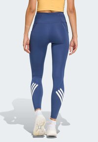 Leggings de sport bleu marine à taille haute, coupe ajustée, tissu texturé et bandes blanches accentuées sur le bas des jambes.