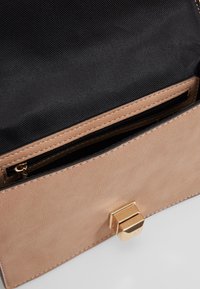 Borsa a mano in faux leather beige con una finitura testurizzata, dotata di un interno in tessuto nero e di una chiusura in metallo dorato. Incluso un taschino con zip.