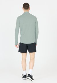 Lange mouwen, lichtgroen sportshirt met hoge kraag, gecombineerd met zwarte shorts en zwarte sportschoenen. Eenvoudig ontwerp, geen patronen.