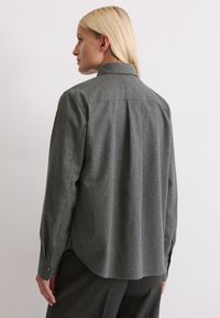 Γκρι πουκάμισο από μείγμα μαλλιού με κλασικό γιακά, μακριά μανίκια και κουμπιά στους καρπούς. Περιέχει καμπυλωτό στρίφωμα και πτυχή στην πλάτη για ευκολία κινήσεων.