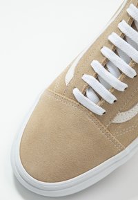 Baskets en daim beige avec lacets blancs et semelle en caoutchouc blanche, vues en gros plan sur l'avant du pied et le côté.