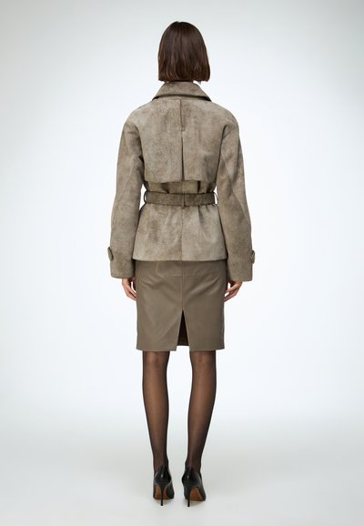 Világosbarna szarvasbőr dzseki övvel a deréknál és széles gallérral, amelyhez egy testhezálló olívazöld műbőr szoknyát párosítottak, hátul sliccel. Fekete magas sarkú cipő.