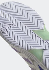 Podeszwa butów Adidas charakteryzuje się wzorem w jodełkę w białym kolorze z zielonym akcentem. Chropowata powierzchnia zapewnia przyczepność i stabilność.