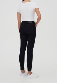 Černé úzké džíny s vysokým pasem, pěti kapsami a hladkou texturou, doplněné bílými teniskami s holografickým akcentem.