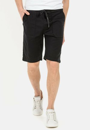 Schwarze Denim-Shorts mit Kordelzugbund, Seitentaschen und lockerer Passform. Kombiniert mit weißen Sneakern für einen lässigen Look.