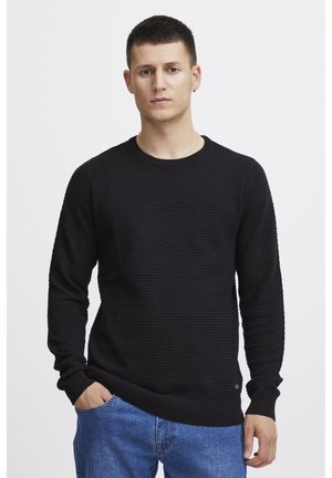 Schwarzer Strickpullover mit strukturiertem Muster, runder Ausschnitt und langen Ärmeln, kombiniert mit blauen Jeans. Einfaches Design mit gerippten Bündchen.
