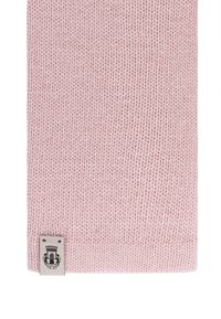 Helle rosa Strickware mit einem kleinen rechteckigen Etikett, auf dem ein schwarzes Emblem und eine Krone nahe der unteren Kante aufgestickt sind.