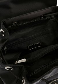 Zwarte stoffen tas met een trekkoordsluiting. Binnenin bevinden zich meerdere met rits afgesloten compartimenten en een merklabel met witte stikselaccenten.