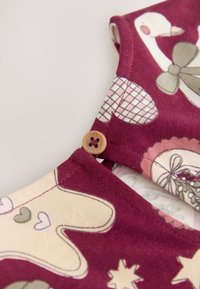 Vinrött tyg med mönster av djur och hjärtan, med en knappdetalj vid halsen. Mjuk textur och bomullsmaterial.