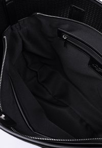 Svart vävd väskas insida som visar en slät svart tygfoder, en zippered ficka och en rymlig design utan synliga mönster eller detaljer.