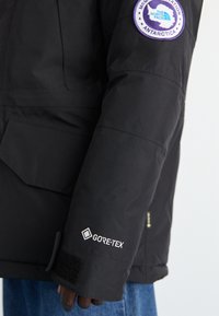 Czarna wodoodporna parka z oznakowaniem GORE-TEX, z naszywką na rękawie. Teksturowana tkanina, mankiety na rzepy i boczna kieszeń.