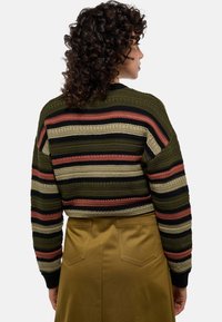 Pull en tricot rayé en olive, noir et rouille avec un design court et une texture chunky. Assorti à un pantalon chino taille haute couleur kaki.