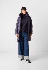 Donkerpaarse pufferjack met capuchon, voorzien van een rits en elastische manchetten. Gecombineerd met donkere, wijde jeans met een rafelige zoom.