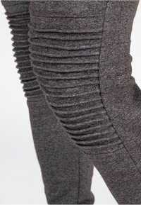 Grå slim-fit bukser lavet af blødt stof, med lodrette ribbede detaljer på siderne, der giver et tekstureret udseende.