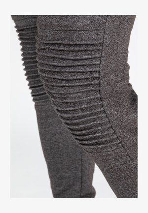 Grijze, aansluitende broek van zacht materiaal, met verticale ribbel details aan de zijkanten die een gestructureerd uiterlijk geven.