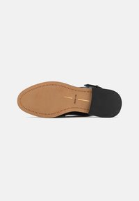 Black shoe sole with a tan leather bottom, featuring a textured rubber area at the heel. Stitched detailing along the edge.