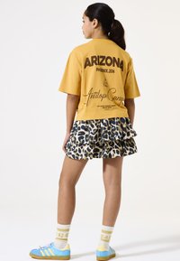 Camiseta amarilla de manga corta con texto negro, combinada con una falda de leopardo con volantes. Zapatos azul claro con acentos amarillos y calcetines blancos.