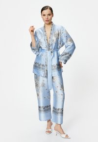 Blå satin tvådelad pyjamas-set med blommönster och detaljerade fållar, med en bälte-knuten wrap-top och vida byxor.