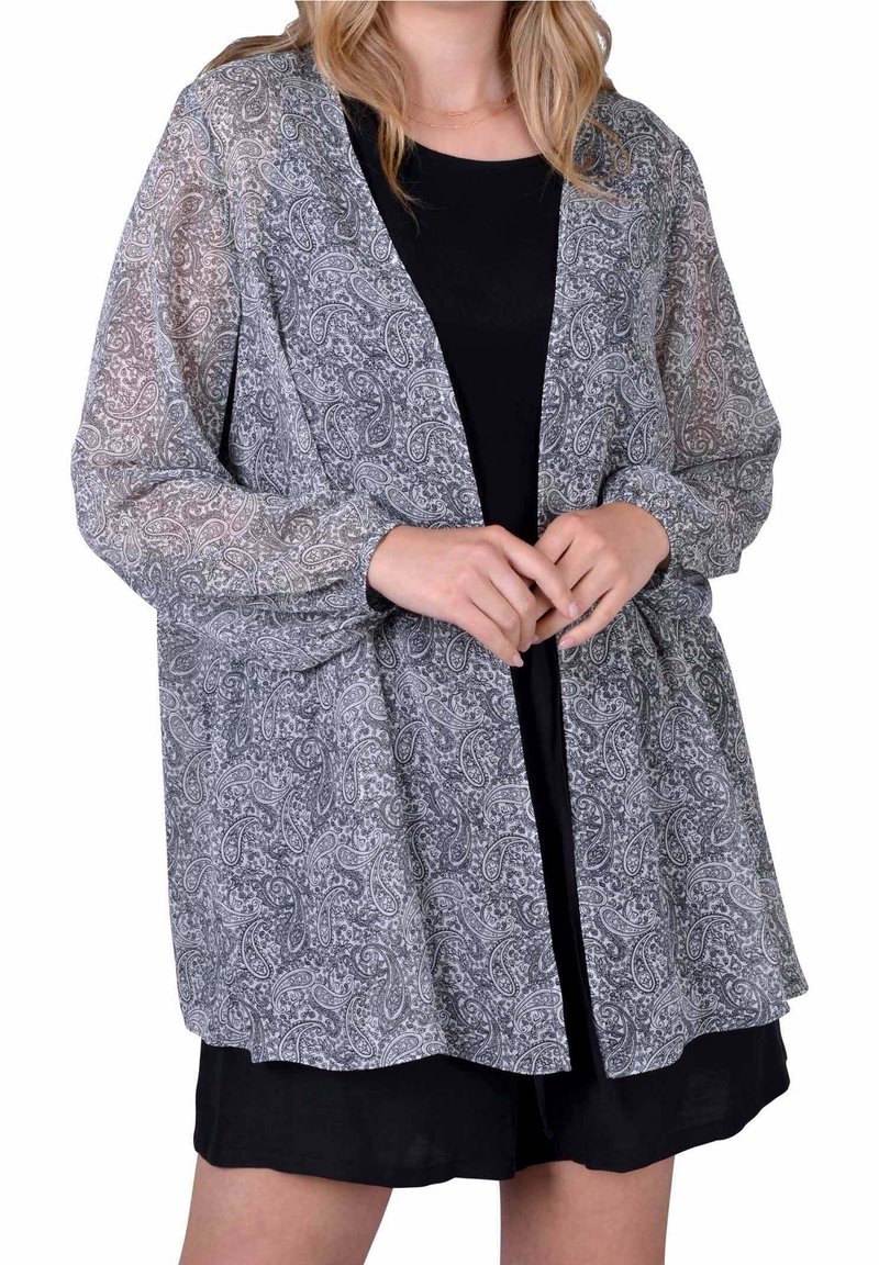 Průsvitná šedá bunda s paisley vzorem, s dlouhými rukávy a volným střihem. Nošeno přes černý top a kraťasy.