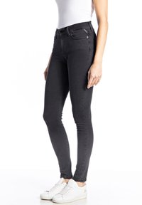 Musta farkkutyyppiset kapeat housut, joissa on korkea vyötärö, vetoketjusepalus ja nappikiinnitys, etutaskut ja sileä pinta. Asustettu valkoisilla lenkkareilla.