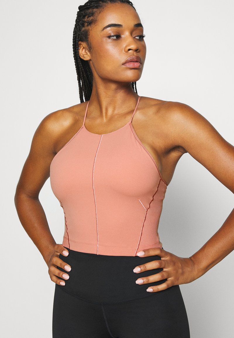 Top atlético ajustado de color rosa claro con tirantes finos y costuras en contraste, combinado con leggings negros de cintura alta para un aspecto elegante.