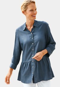 Dunkelblauses Denim-Peplum-Hemd mit Knopfleiste, Punktkragen und Dreiviertelärmeln. Mit Falten an der Taille und glatter Textur.