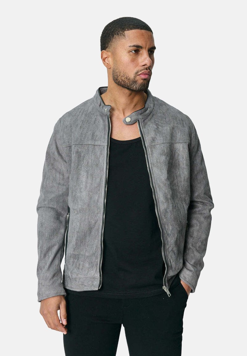 Veste en suédine grise avec col montant, fermeture éclair sur toute la longueur, poches latérales et texture lisse, associée à un t-shirt noir en dessous.