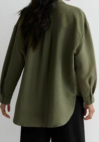 Olivgrön oversized skjorta med en texturerad finish, långa ärmar, knappmanchetter och rundad nederkant. Bärs med mörka byxor.