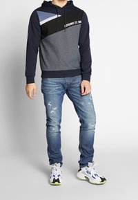 Huvtröja med en färgblockdesign i blått, grått och svart. Återförenad med slitna ljusblå jeans och vita sneakers.