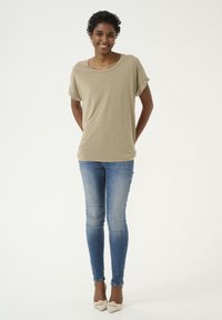 Beige, rövid ujjú felső, kerek nyakkivágással, világoskék skinny farmernadrággal párosítva. A model a tejszín színű hegyes orrú balerinacipőt visel.