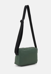 Grøn rektangulær crossbody taske med lynlås, polstret materiale og en justerbar sort rem. Glat tekstur og minimalistisk design.