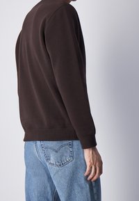 Felpa marrone con scollo rotondo e polsini a costine, abbinata a jeans di denim azzurro chiaro con classico design a cinque tasche.