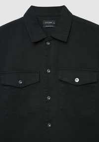 Schwarzes Jeanshemd mit spitzem Kragen, silbernen Druckknöpfen und zwei vorderen Taschen mit Klappenverschluss. Regular Fit.