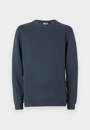 Tumši zilas krāsas krekls ar piegriezumu, izgatavots no gludas auduma, ar garām piedurknēm un ribinātām aprocēm. Vienkāršs dizains, bez rakstiem vai grafikas.