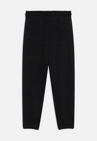 Pantalons de survêtement noirs en coton doux avec une taille élastique, des jambes fuselées et une poche arrière unique. Texture lisse, sans motifs visibles.