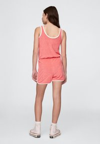 Korallfärgade shorts i frottétyg med vit kant. Innehåller ett ärmlöst linne och shorts med resår i midjan. Bärs med vita ankelstövlar.