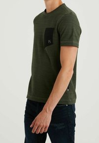Camiseta verde oliva con un acabado texturizado, escote redondo, mangas cortas y un bolsillo en el pecho negro con un detalle de logo.