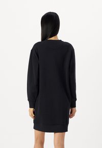 Svart sweatshirtkjole med lange ermer, rund hals og ribbestrikkede mansjetter, med en løs passform og glatt stofftekstur.